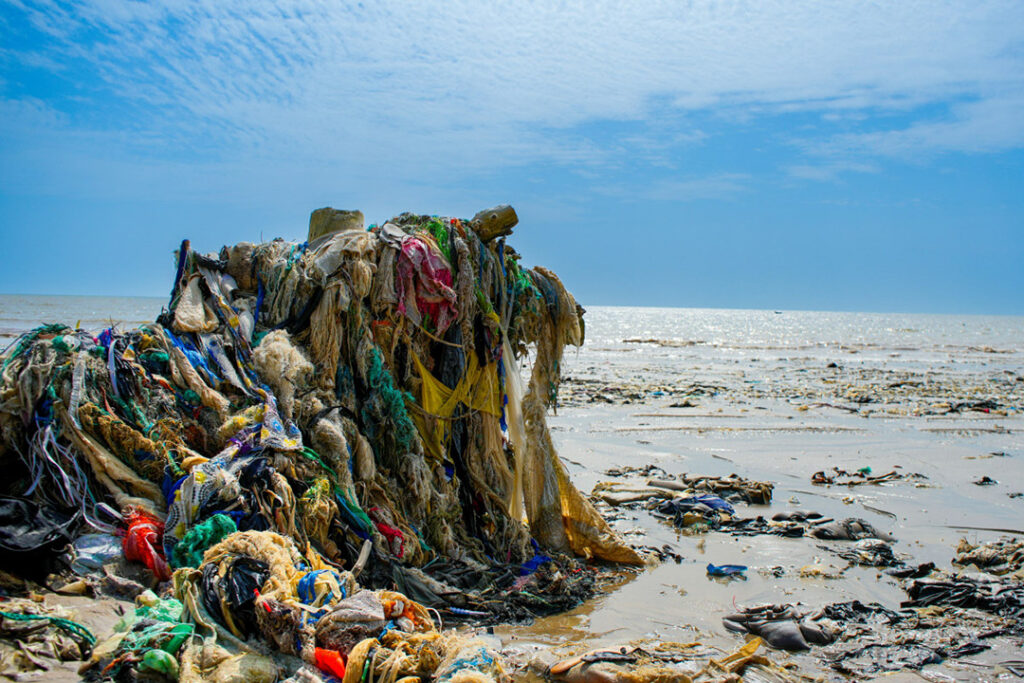 Impatto dell'industria tessile sugli oceani: i rifiuti tessili, come quello raffigurato qui, inquinano i nostri mari e le nostre spiagge, evidenziando l'urgente necessità di adottare pratiche più sostenibili nella produzione e nel consumo di moda. La crescente dipendenza dalle fibre sintetiche e la mancanza di un adeguato riciclo aggravano questa crisi ambientale. 